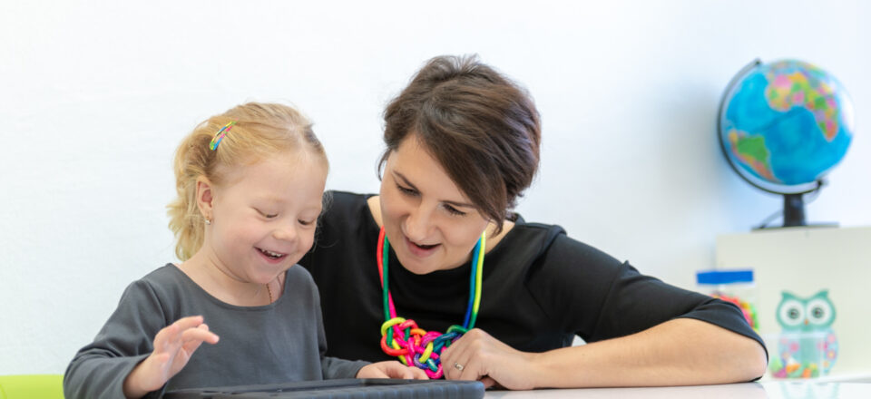 Toddler girl in child occupational therapy session doing playful exercises on a digital tablet with her therapist.
