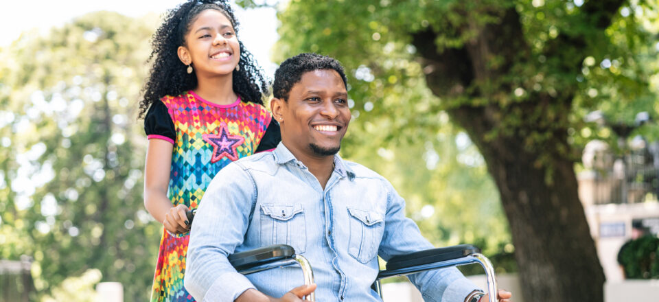 An african american man in a wheelchair enjoying a walk outdoors with his daughter.