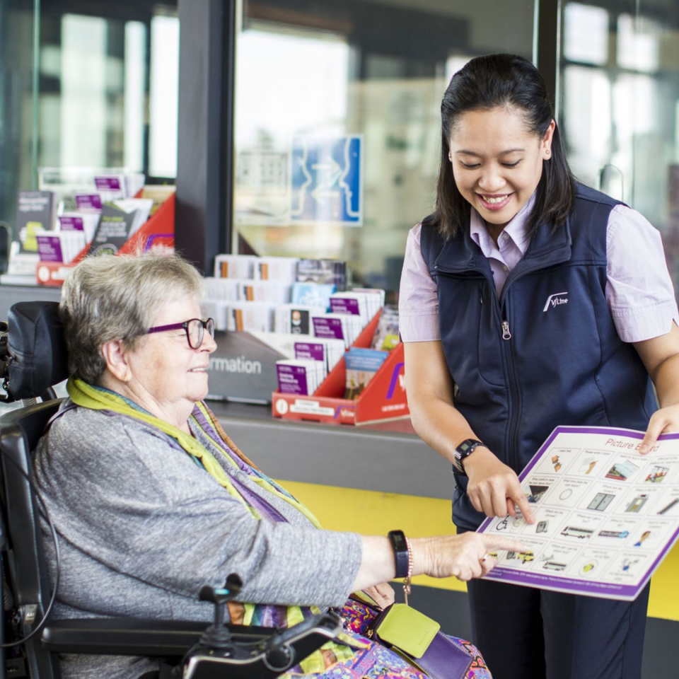 Woman in wheelchair pointing at communication aid held by an employee